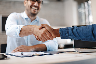 Business owner shaking hands with SEO Ocean County professional over a desk witha clipboard and laptop