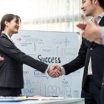The word SUCCESS on a white board behind a branch manager and IRM service professional shaking hands