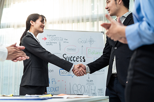 The word SUCCESS on a white board behind a branch manager and IRM service professional shaking hands